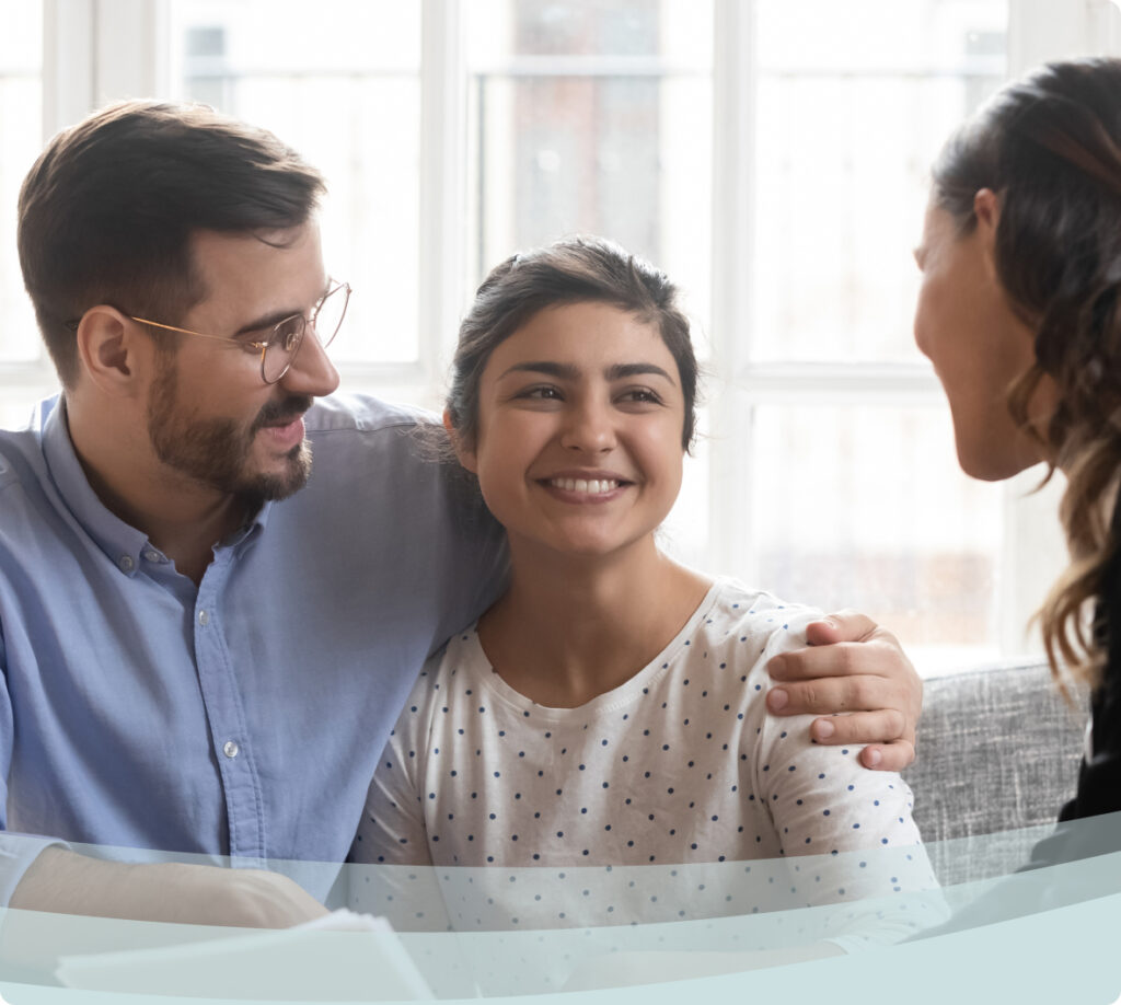 A young couple sitting on a couch chatting with a lawyer.