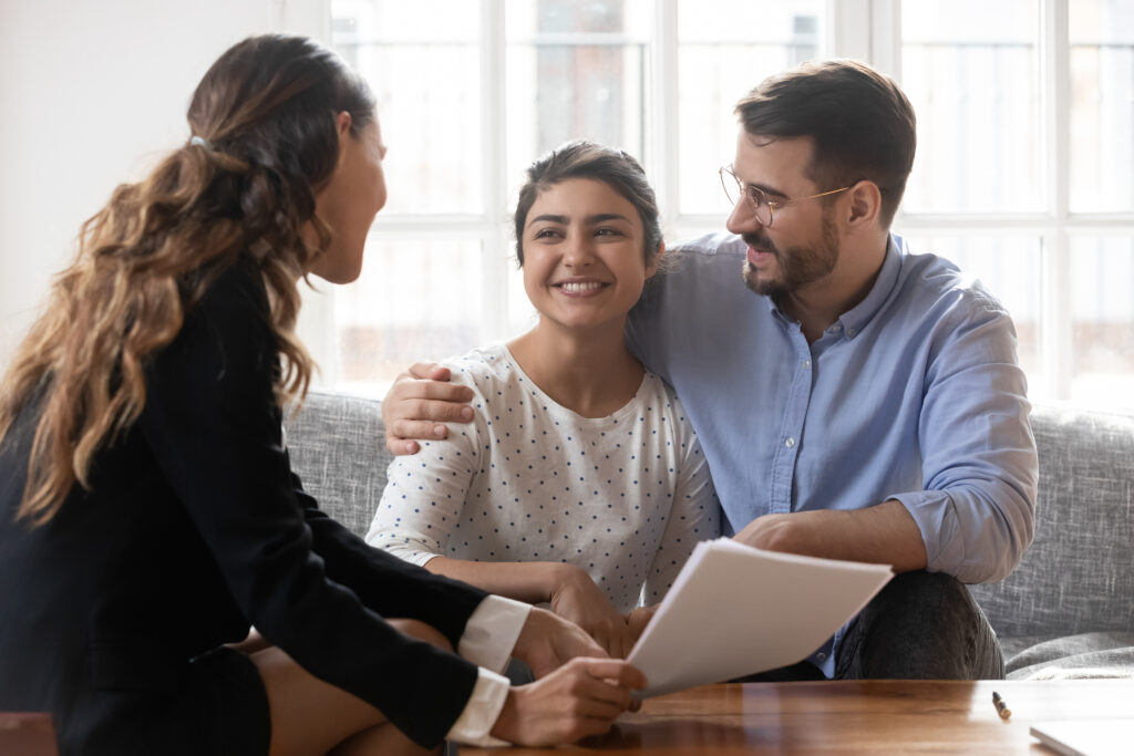A young couple sitting on a couch chatting with a lawyer.